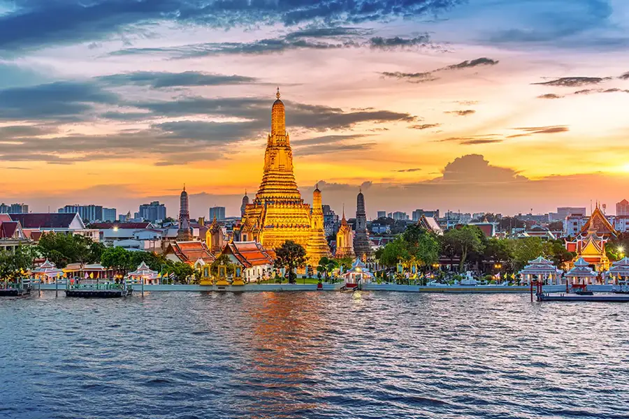 Vista panorámica del templo Wat Arun en Bangkok, Tailandia, al atardecer. El templo budista, con su característica torre dorada, se refleja en el río Chao Phraya.
